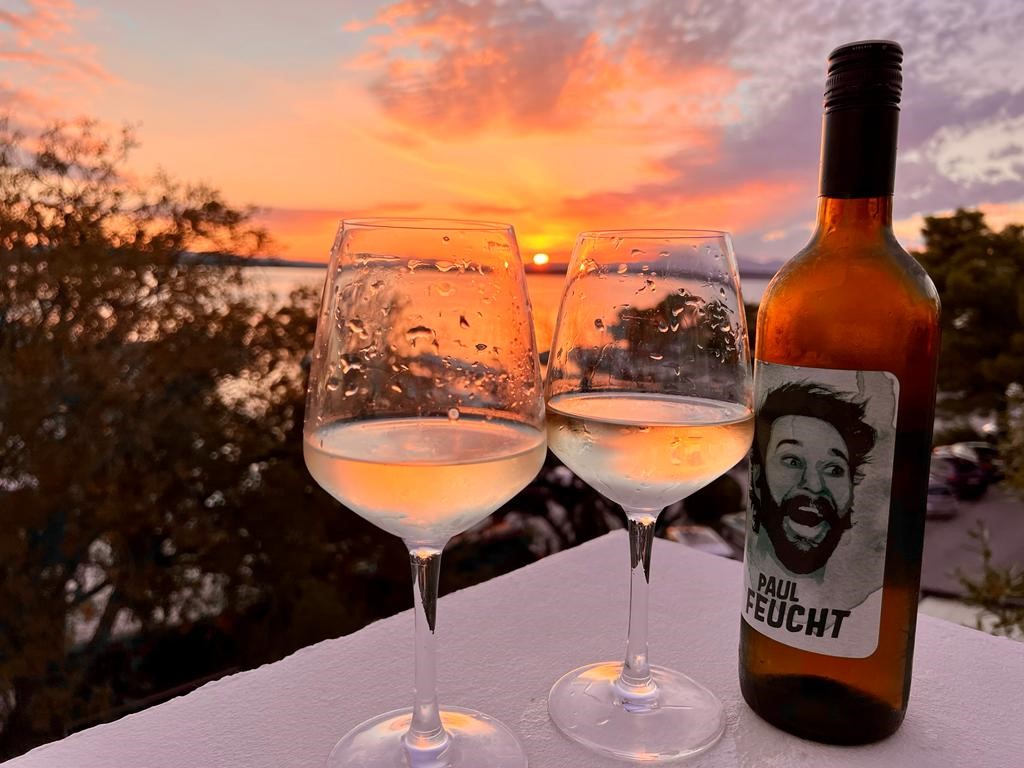 Eine Flasche Paul Feucht mit zwei Gläsern auf einem Tisch. Dahinter ein Sonnenuntergang.