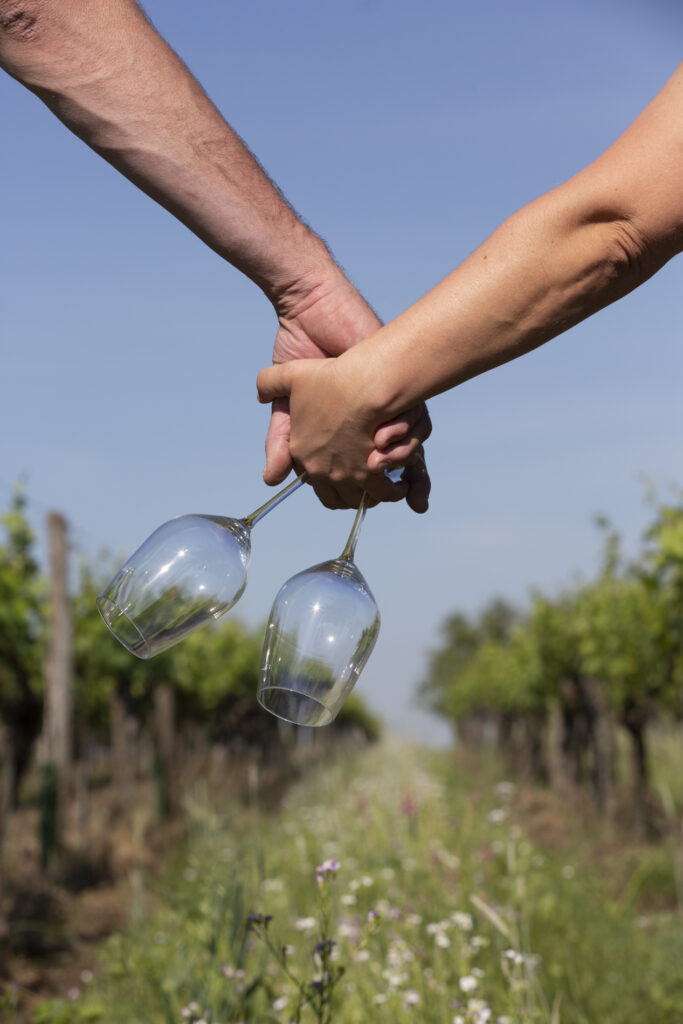 Zwei Hände mit Weingläsern Hand in Hand auf einer grünen Wiese.